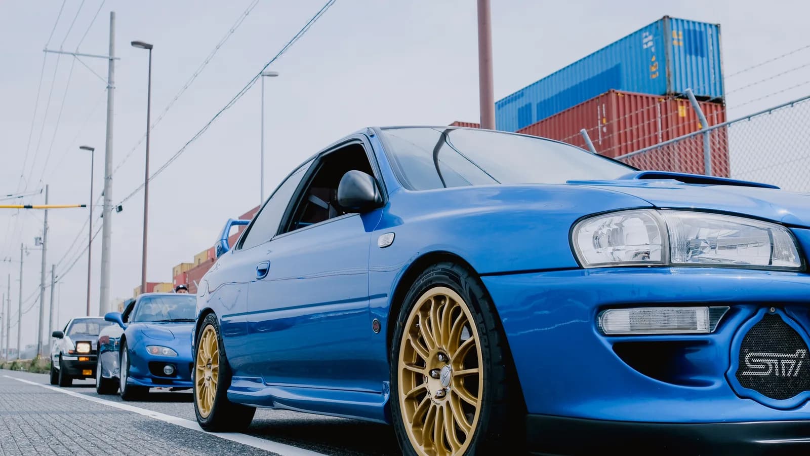 Blue Subaru Impreza parked beside stacked shipping containers