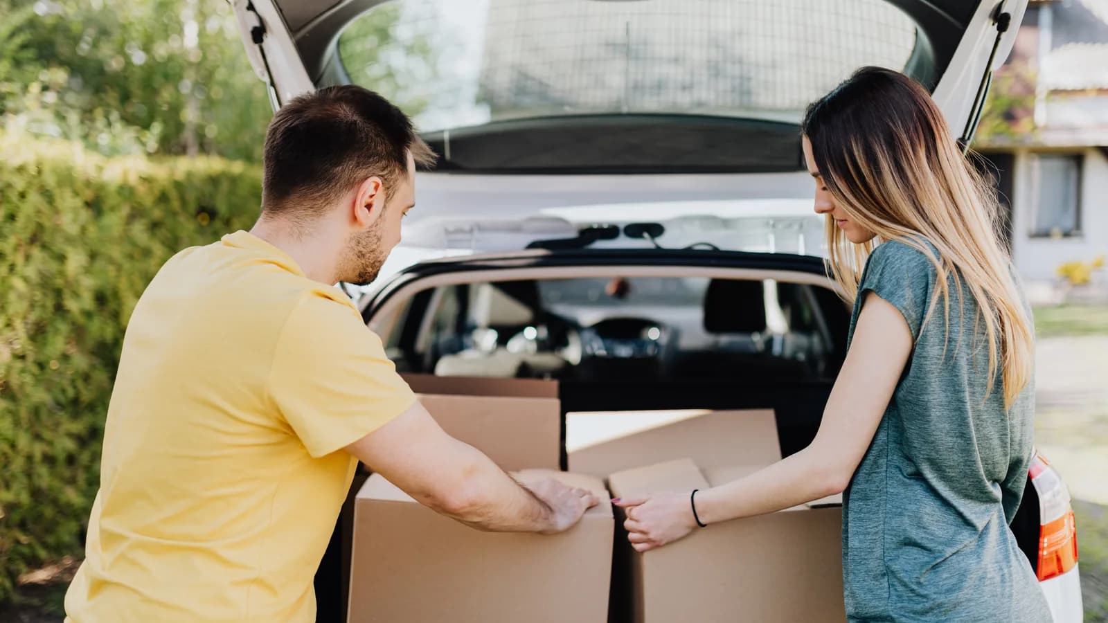 Two people loading cardboard boxes into the open boot of an SUV