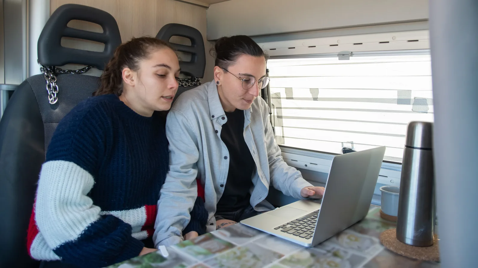Two people sitting at a table inside a campervan looking at a laptop