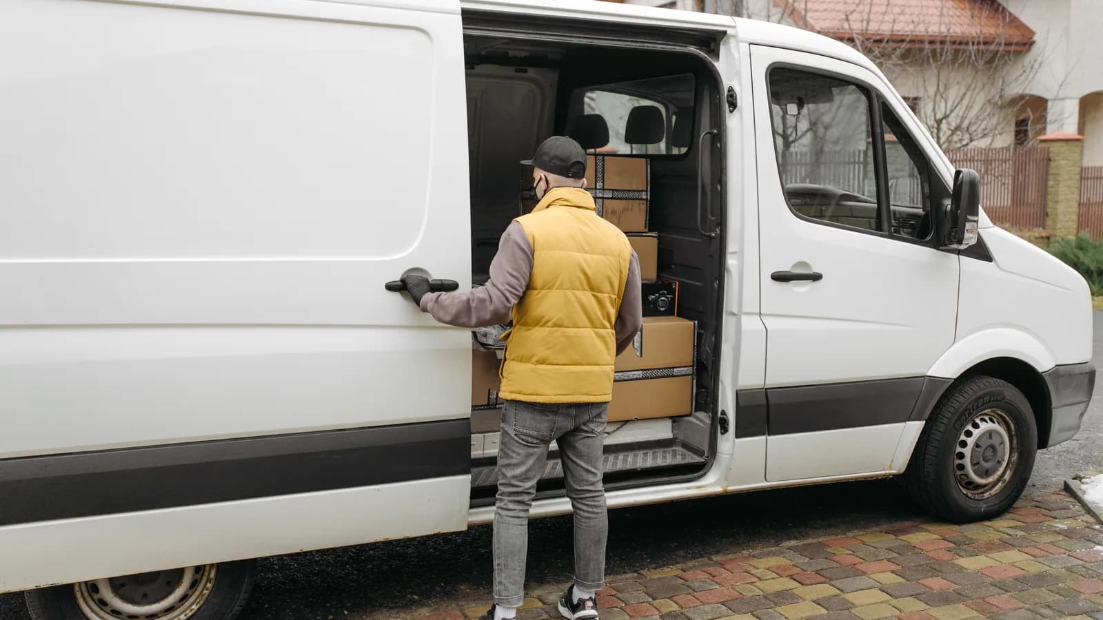 A courier loading boxes through the open side door of a white van on a suburban street