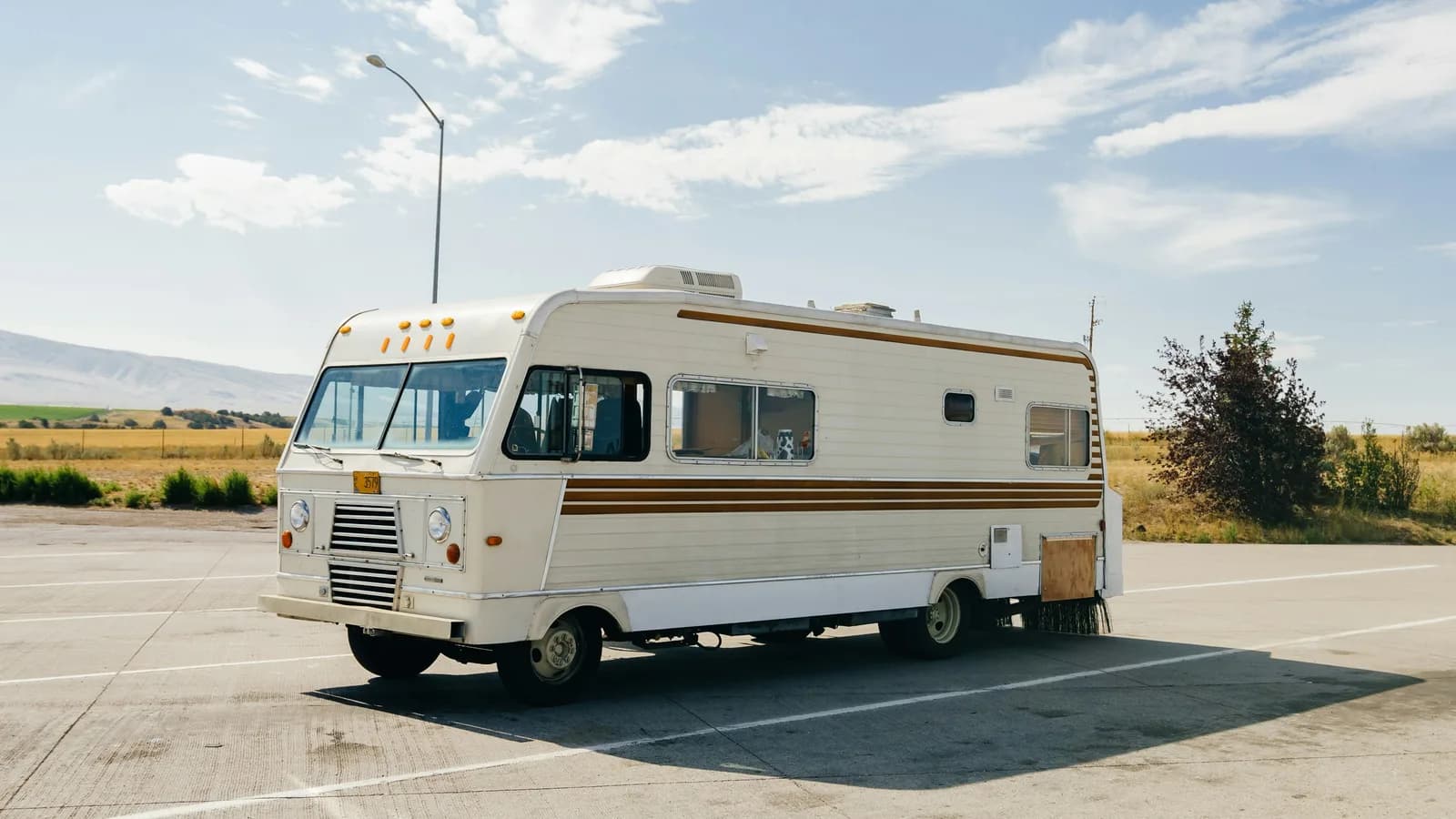 A vintage motorhome parked by itself in an empty sealed car park under a clear sky