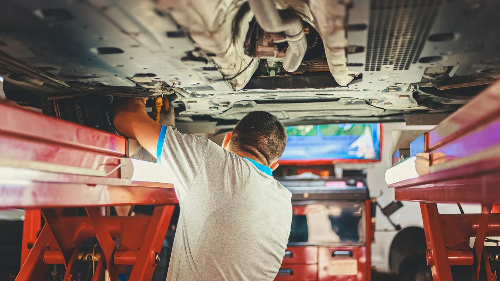 A mechanic looking up at the underbody of a vehicle in a garage