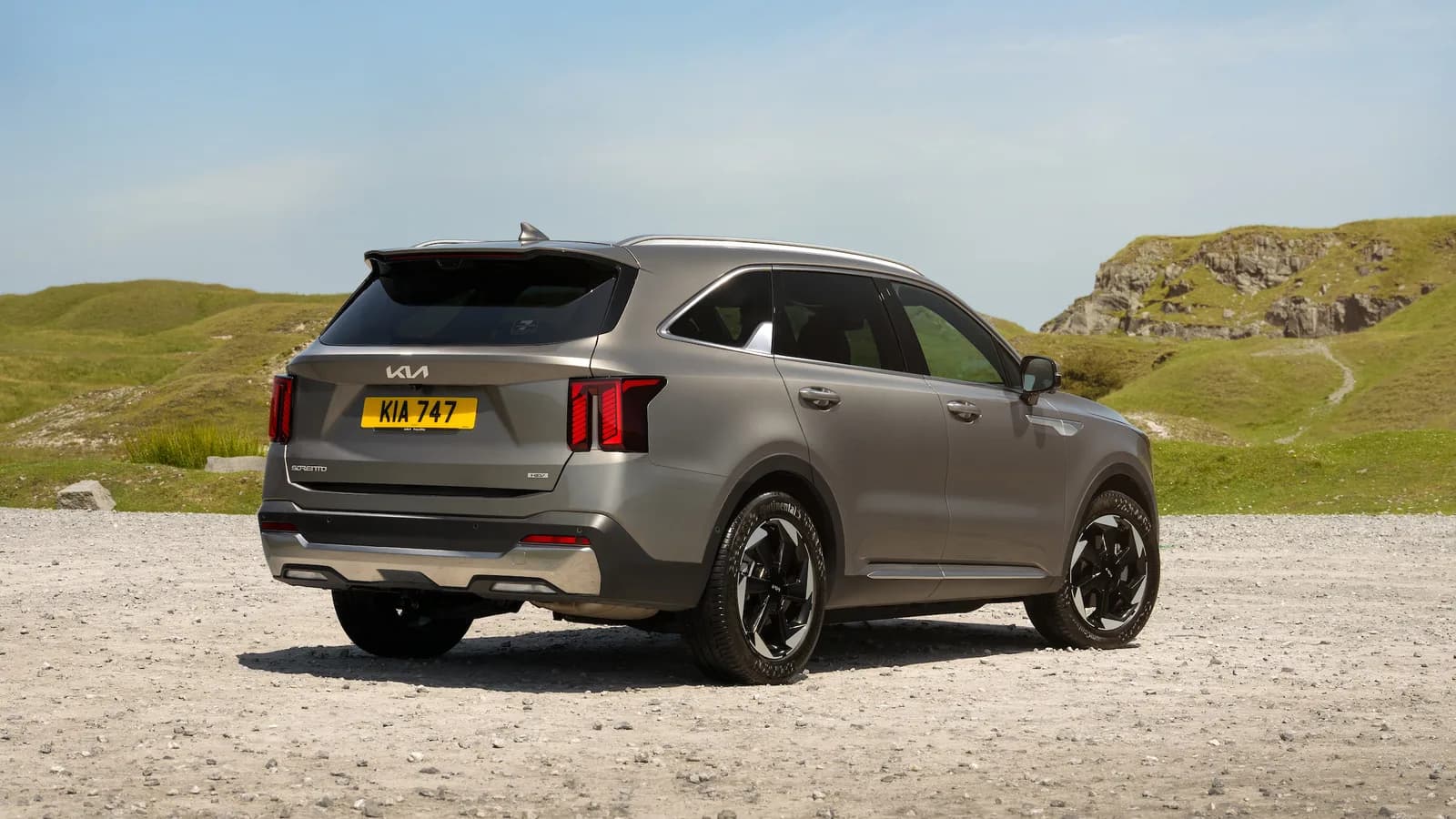 A grey Kia Sorento parked on a gravel track with hills behind it