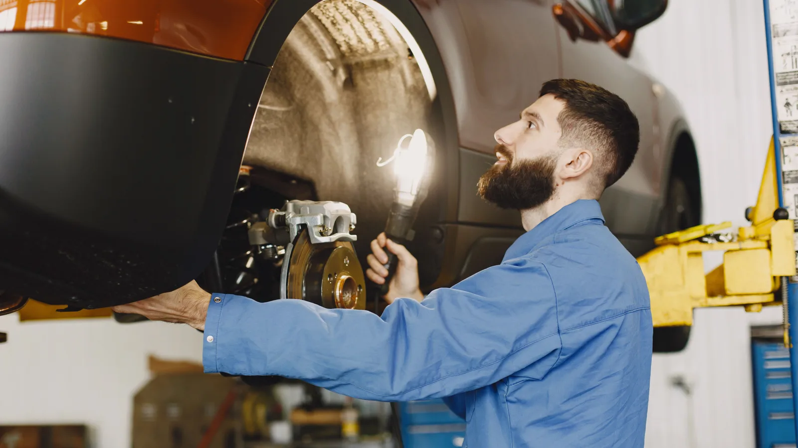 A mechanic inspecting a brake rotor and caliper on a car raised on a workshop hoist