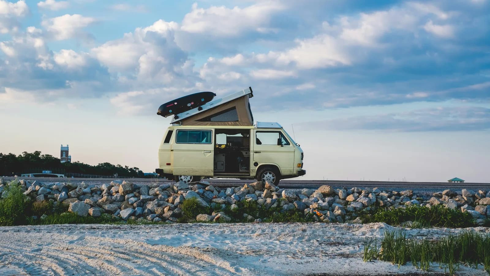 A camper van with a pop-top roof and rooftop box parked on a rocky shoreline