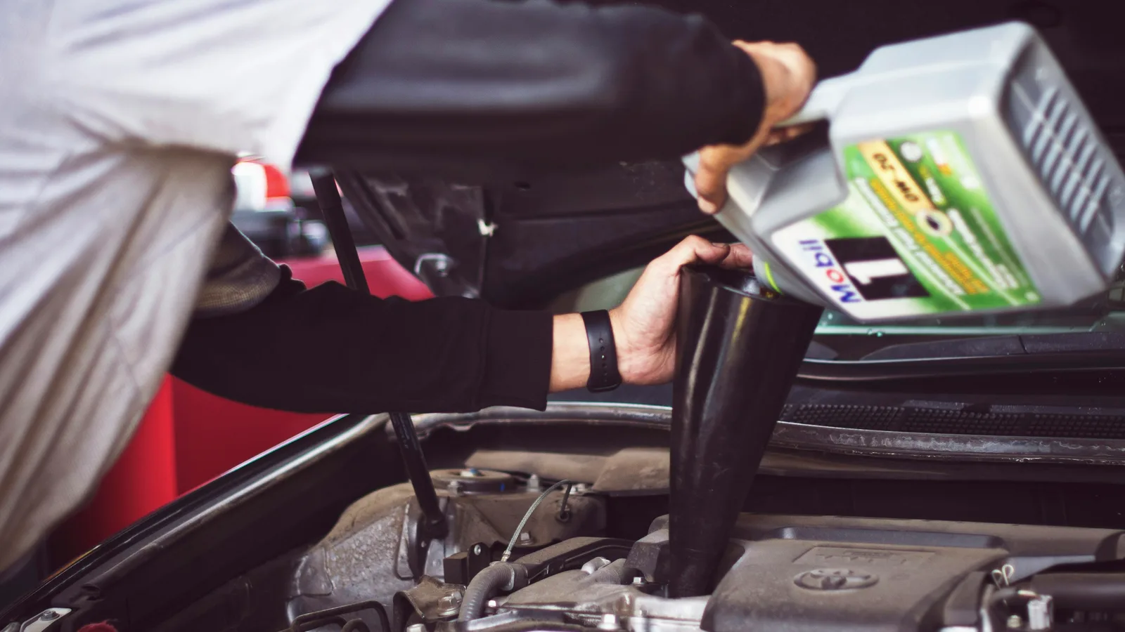 A mechanic pouring engine oil into a Toyota engine bay through a funnel
