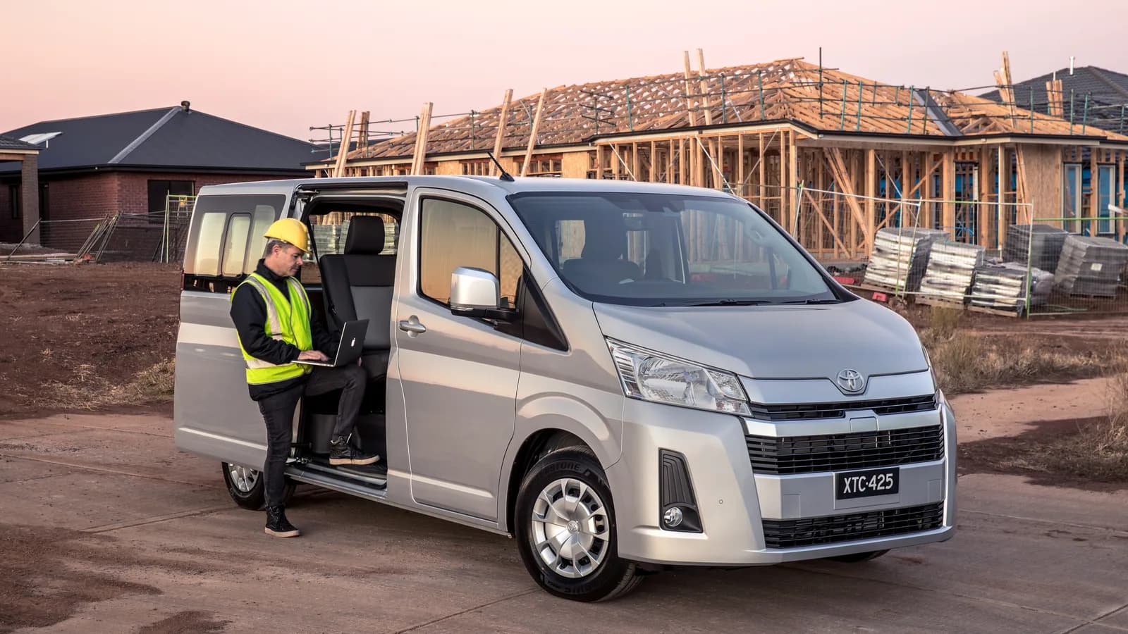 A silver Toyota HiAce parked at a work site with a worker stepping in through the sliding door