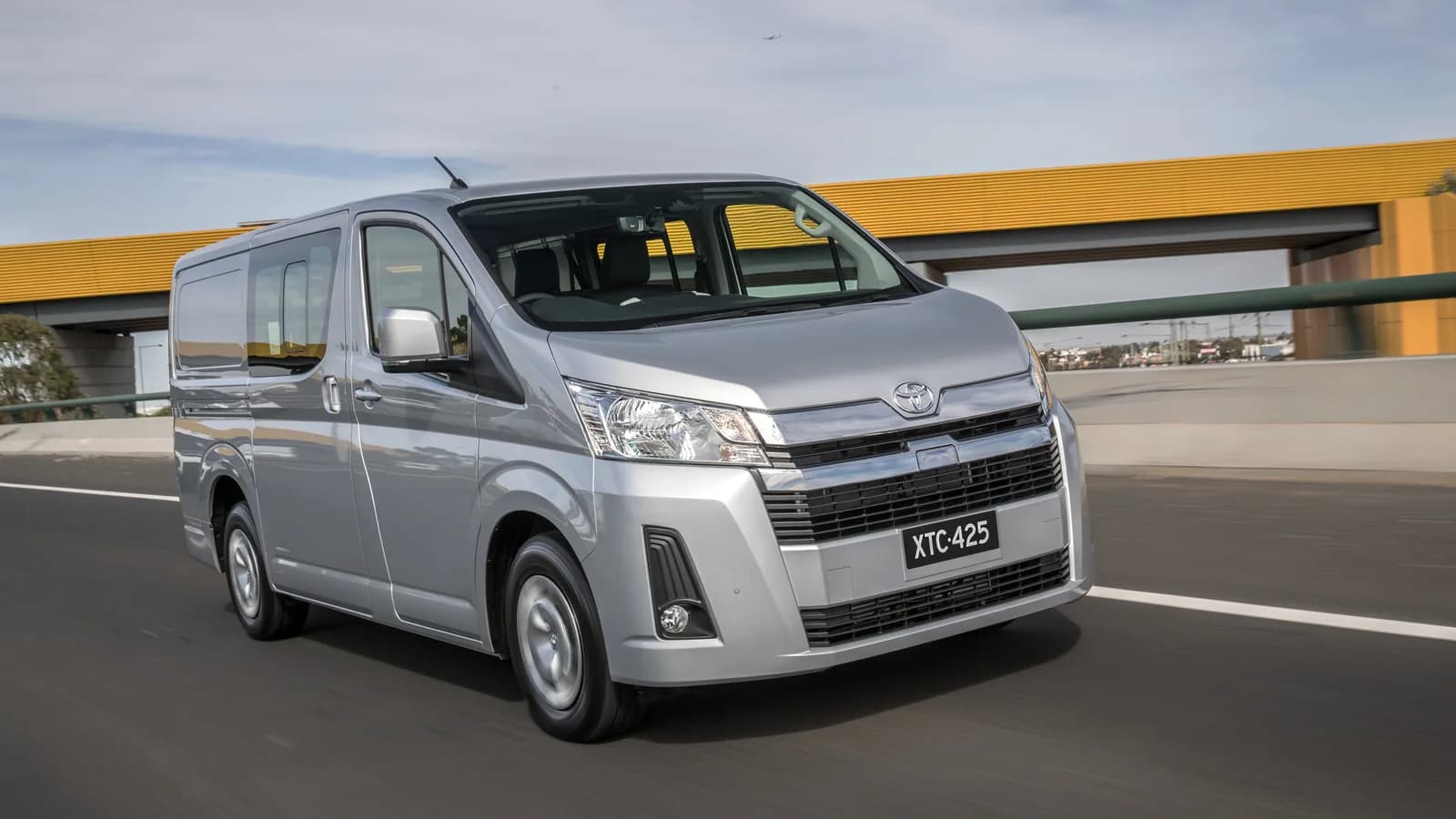 A silver HiAce van travelling on a highway, front three-quarter view