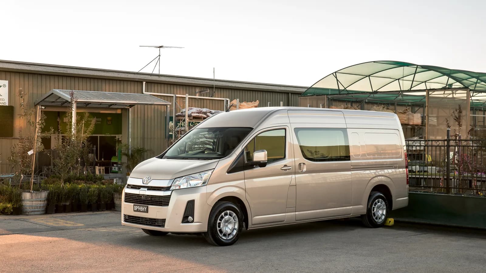 A beige HiAce van parked outside a plant nursery with its front three-quarter visible