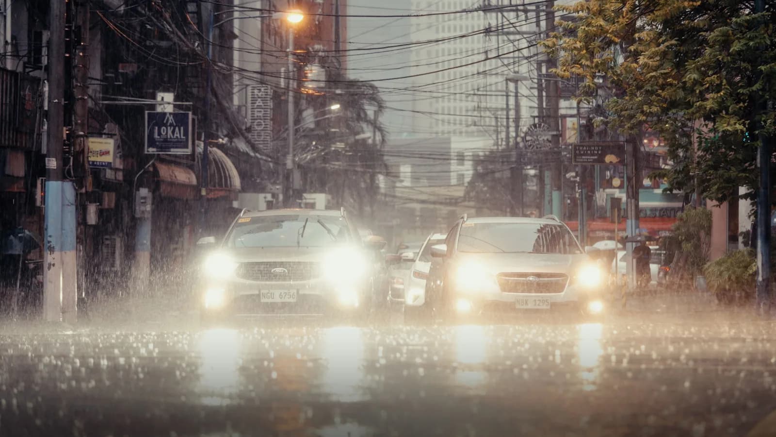 Cars with headlights on crawling through a flooded city street during heavy rain