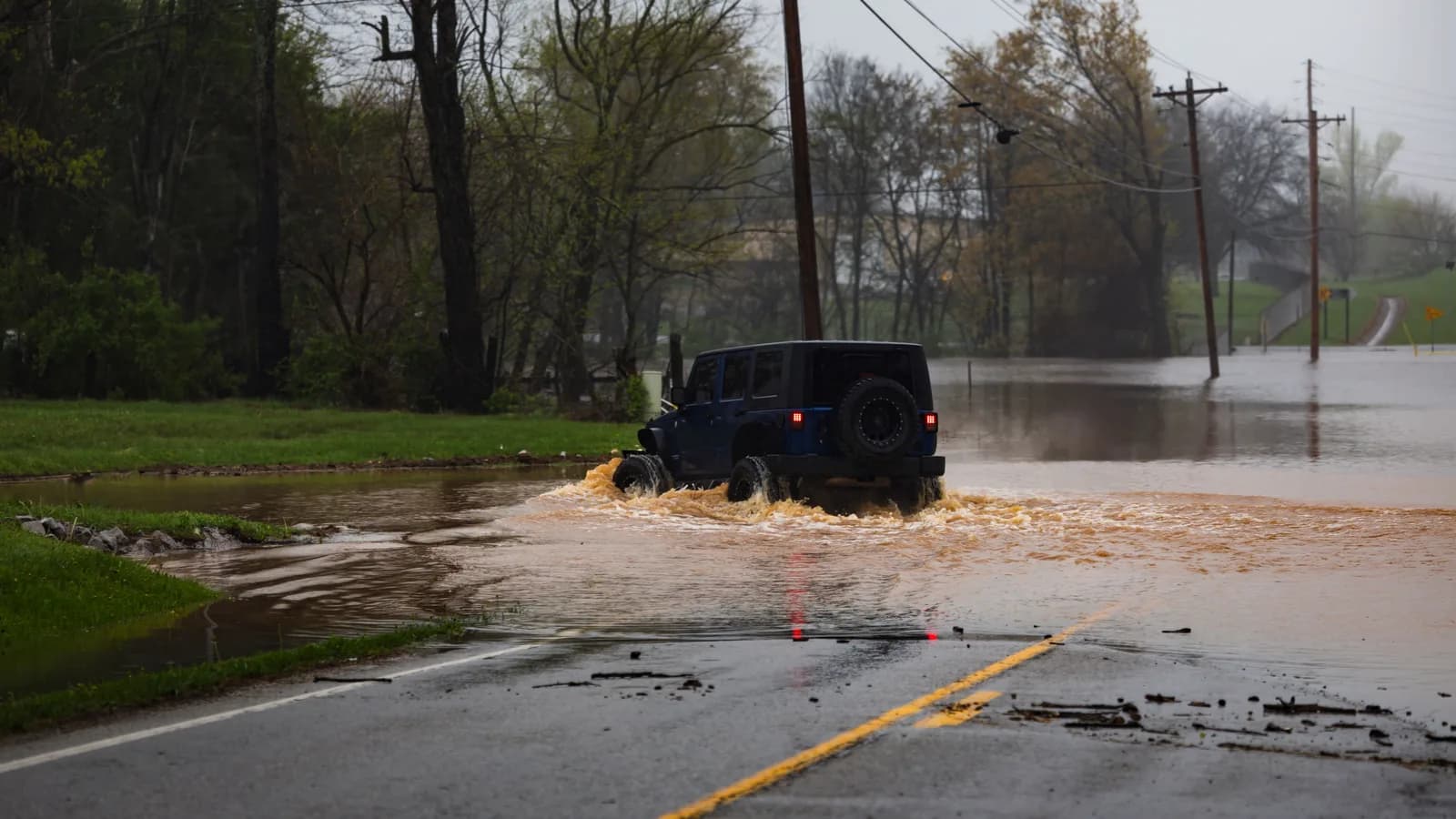 A dark blue four-wheel drive in flooded water that reaches partway up its wheels