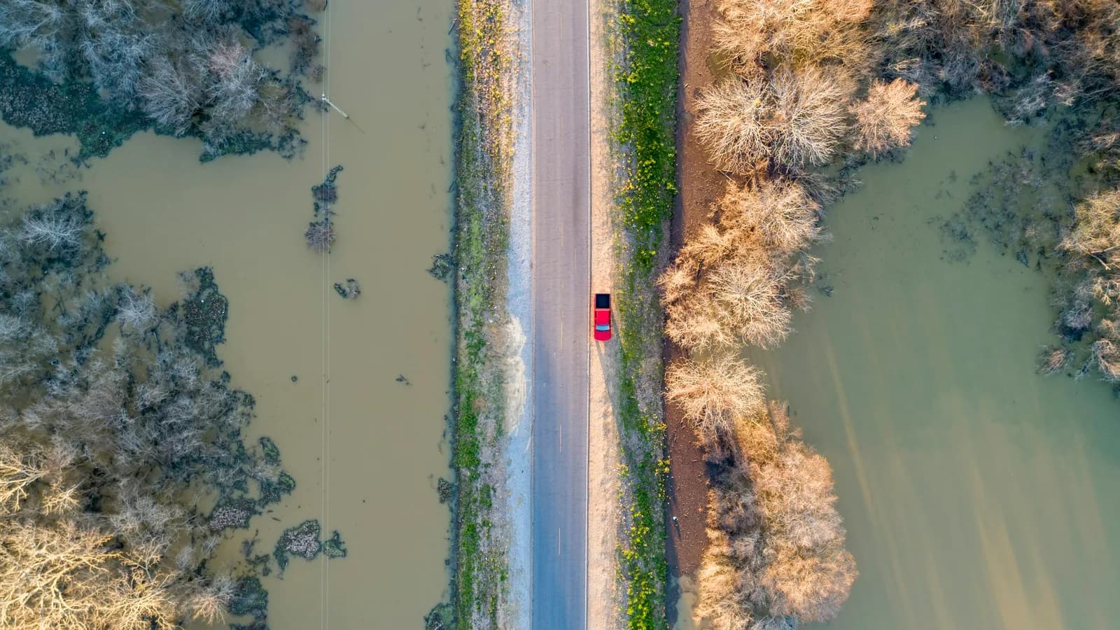 Aerial view of a car stopped on a narrow road with floodwater on both sides