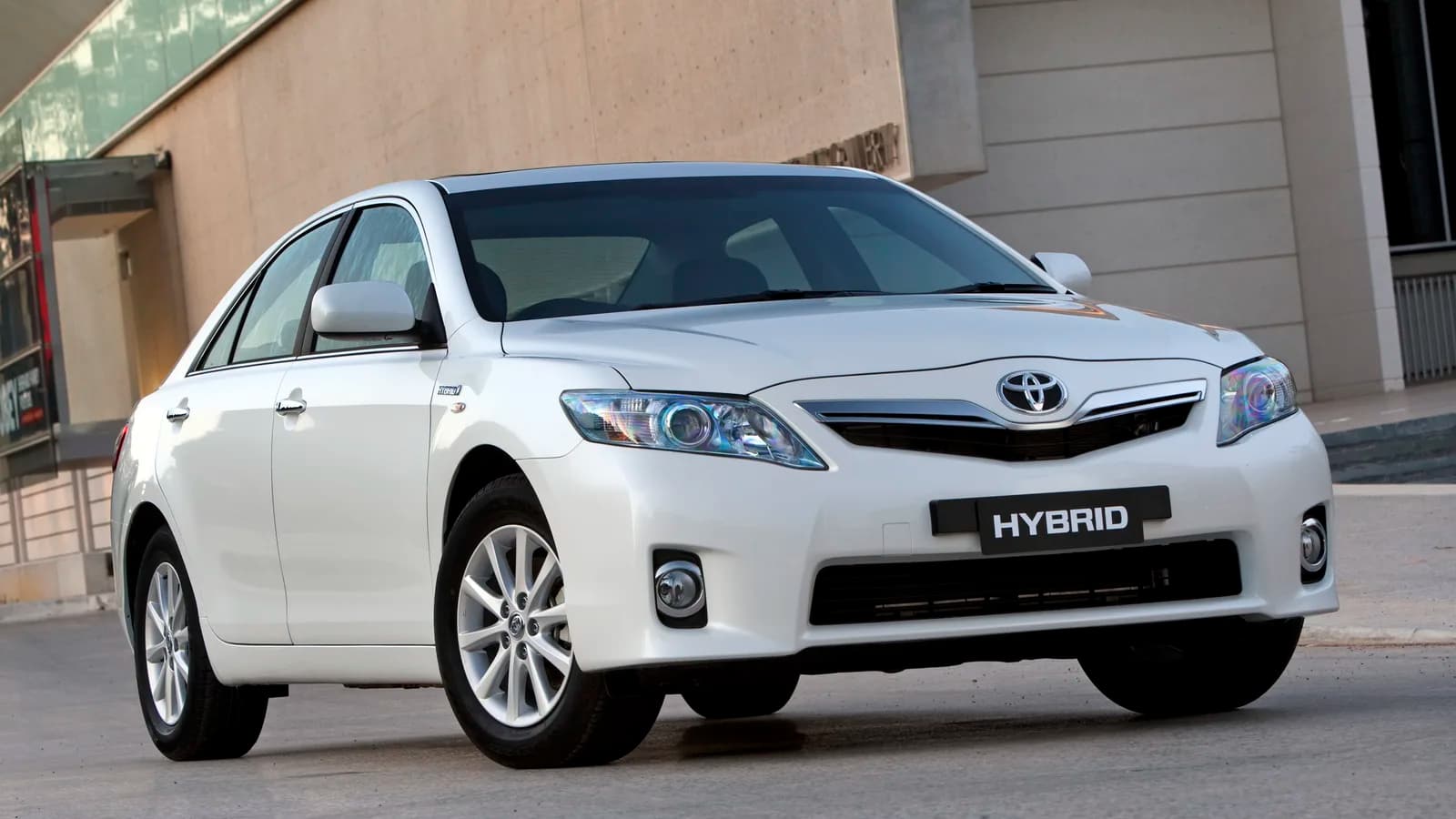 A white Toyota Camry sedan parked at the kerb outside a building