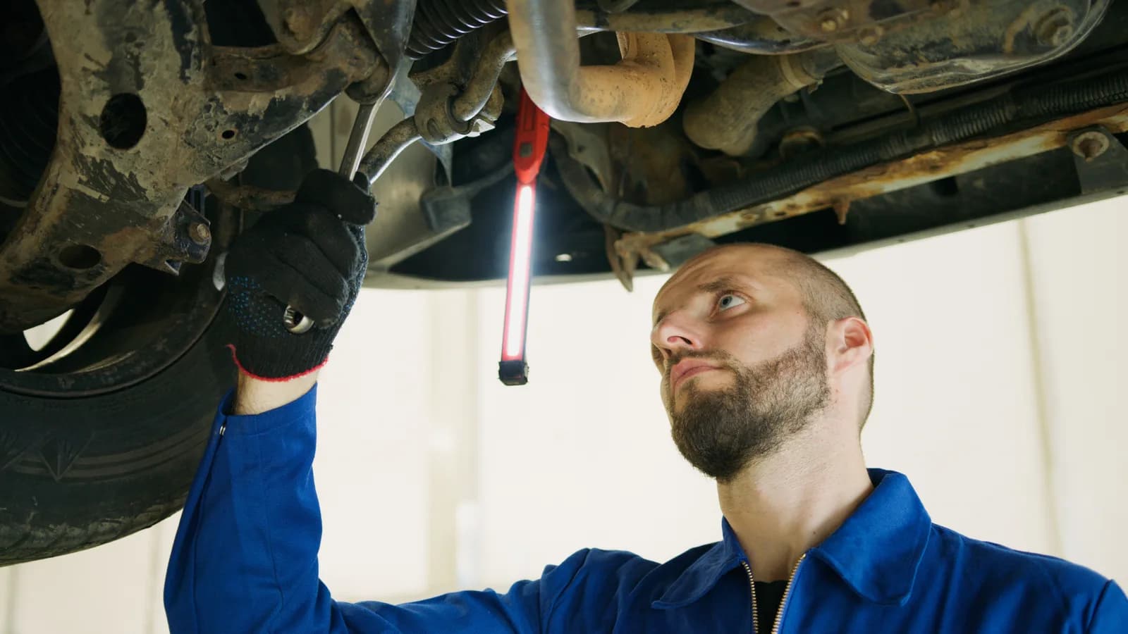 A mechanic under a raised car using a wrench on a suspension component