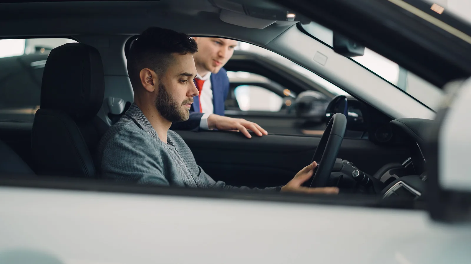 A salesman leaning into a car talking to a man seated in the driver's seat