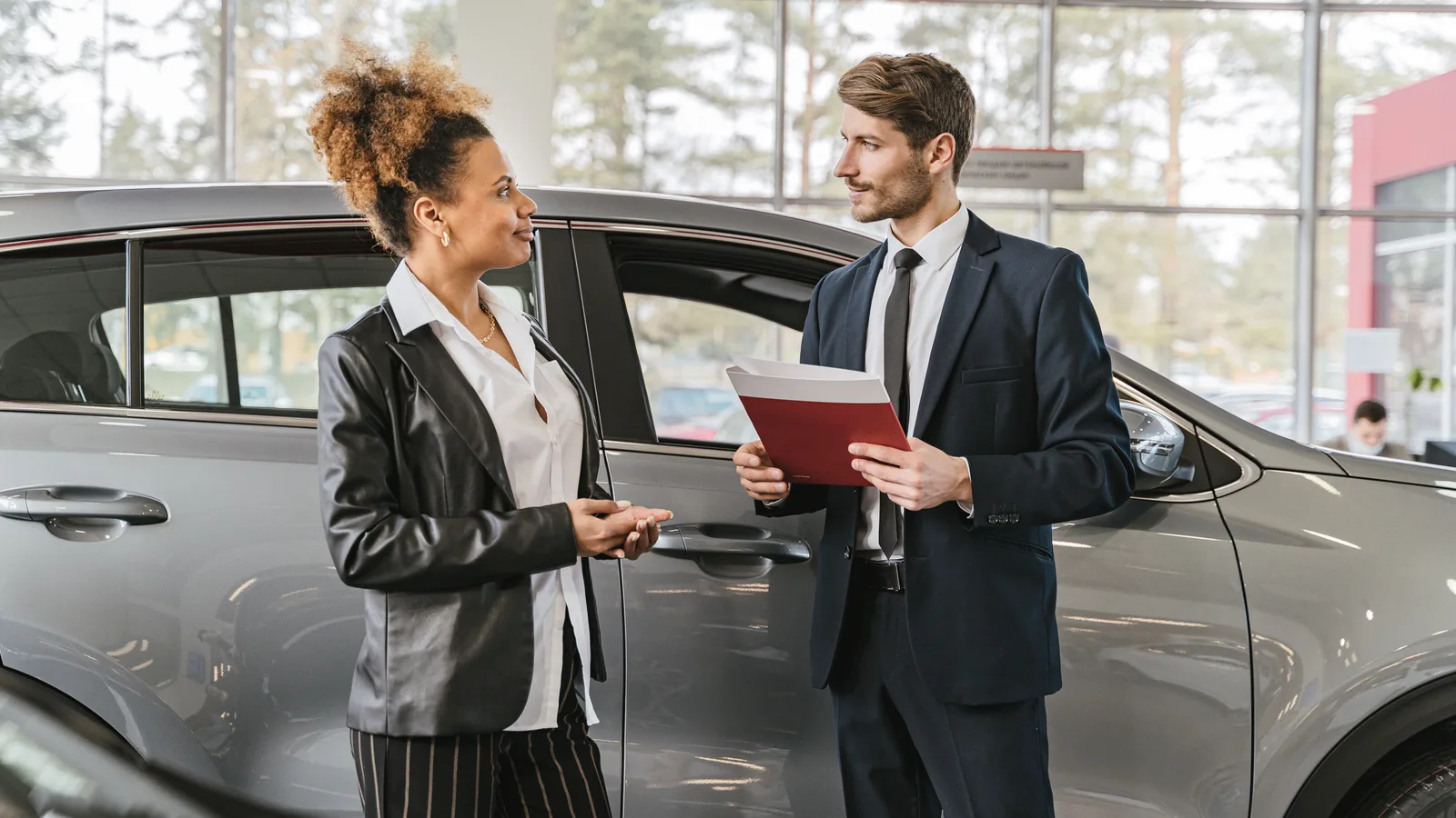 A salesperson handing documents to a customer beside a car at a dealership
