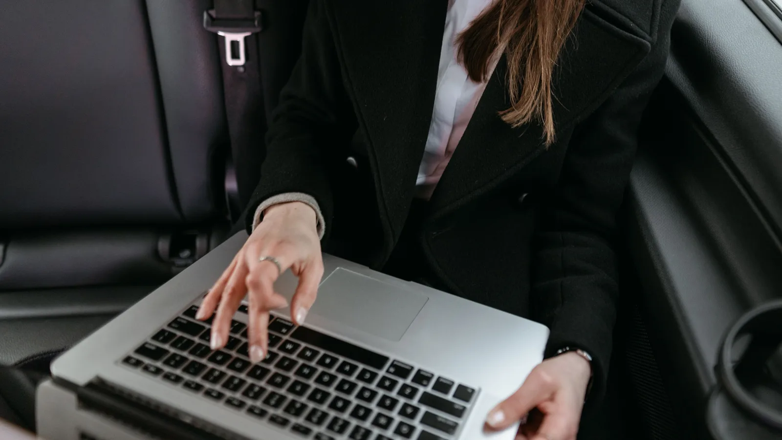 Close-up of two hands typing on a laptop keyboard inside a parked car