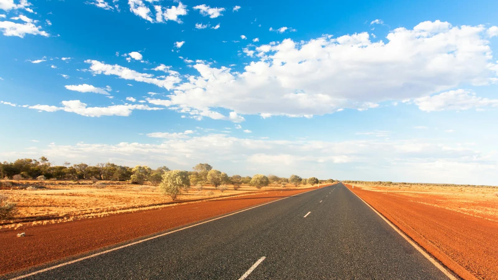 A straight sealed highway with open red-dirt verges on both sides and low scrub beyond