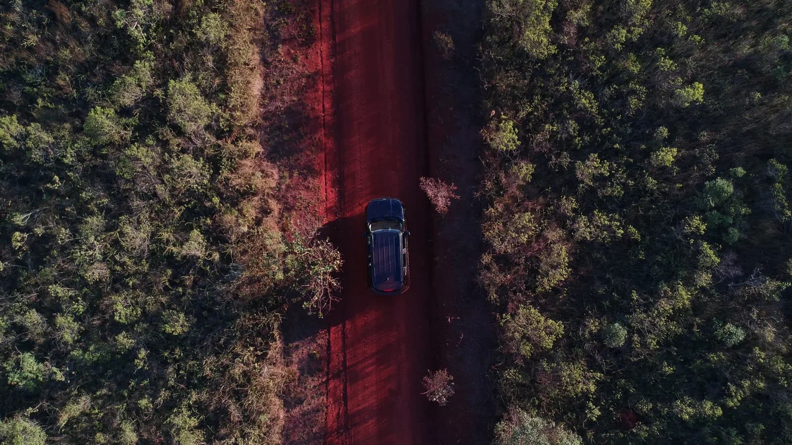 An SUV seen from above driving along a red dirt road through low bushland