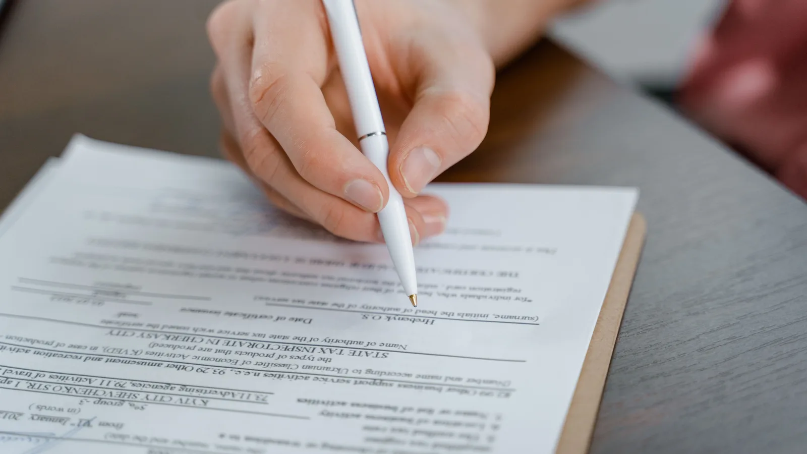 A hand signing a vehicle transfer document with a pen