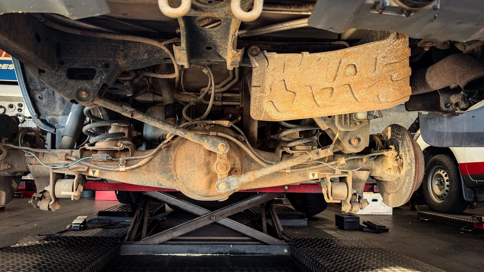 The underside of a van on a hoist showing the rear axle, suspension arms and surface rust