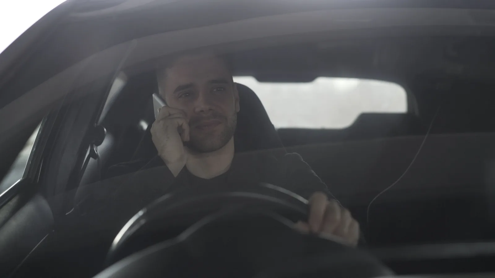 Driver holding a mobile phone to his ear while the car is on the road