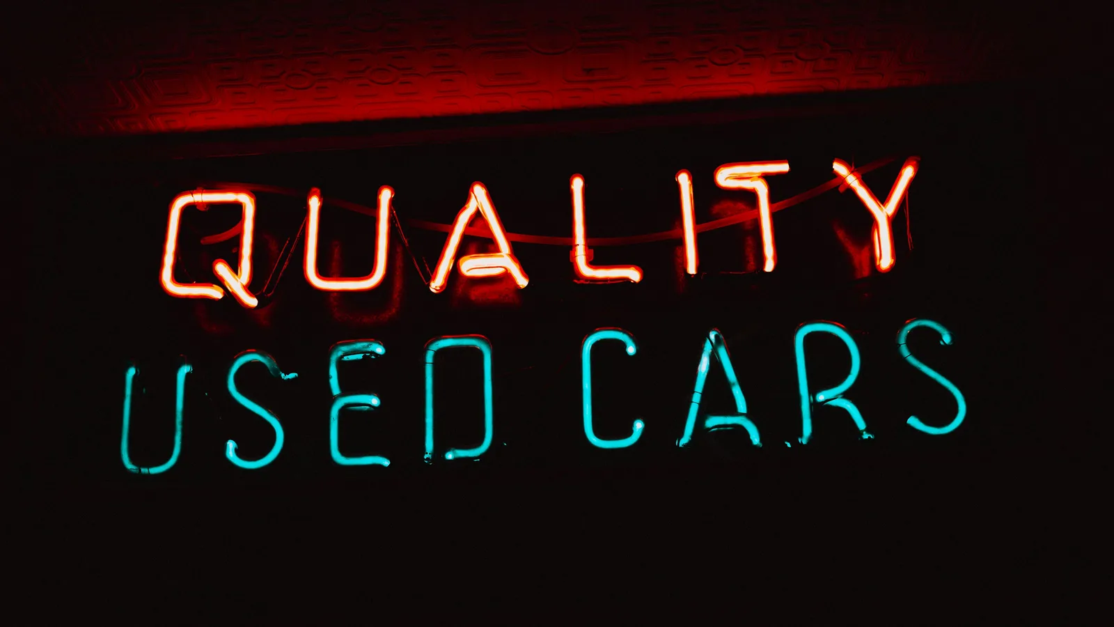 A neon sign reading quality used cars glowing above a dealership lot at night