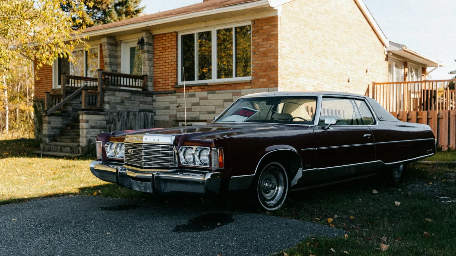 A dark red sedan parked in a driveway with a for sale sign in the windscreen