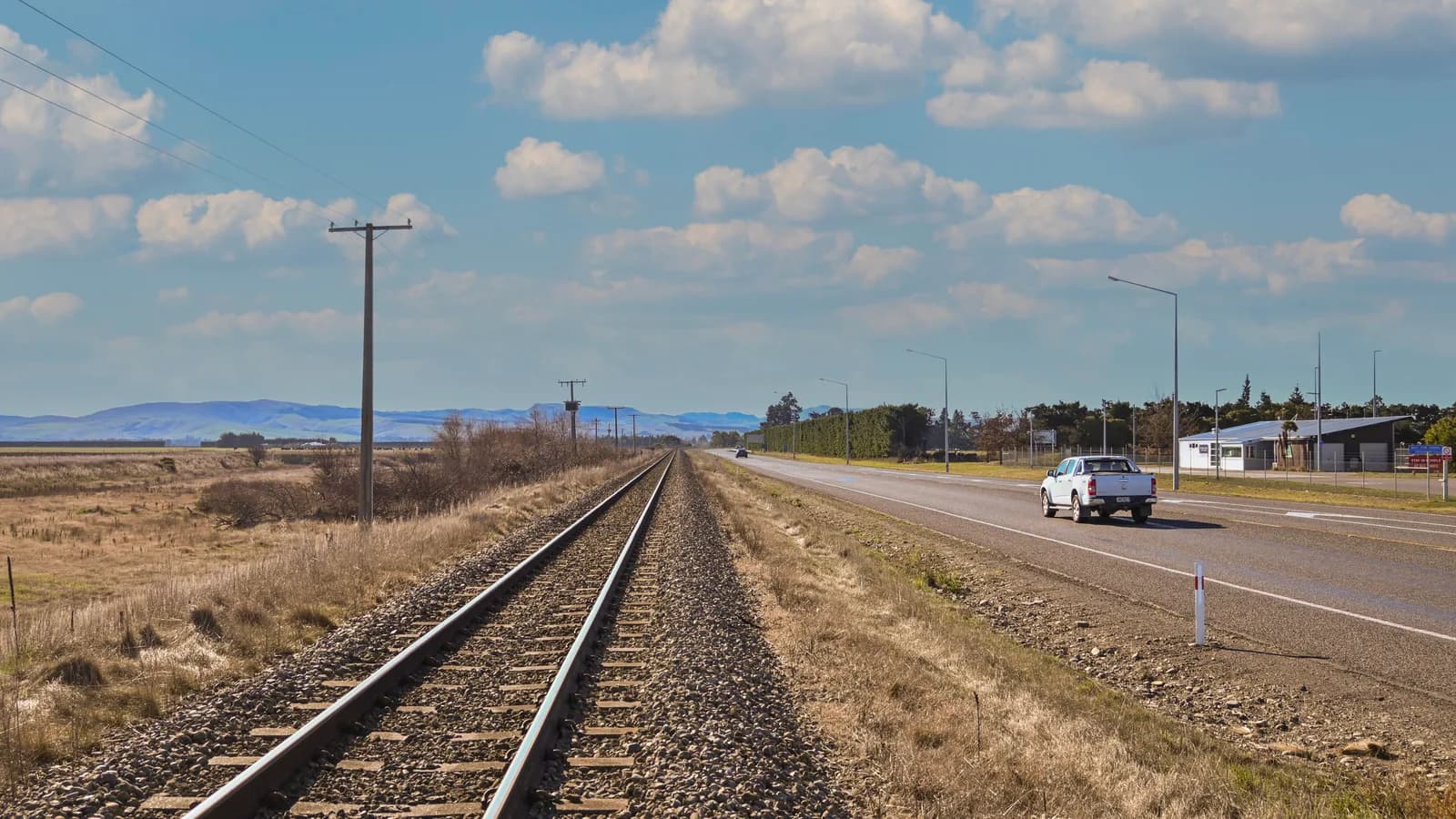 A ute travelling along a straight two-lane regional highway with open country and clear road ahead