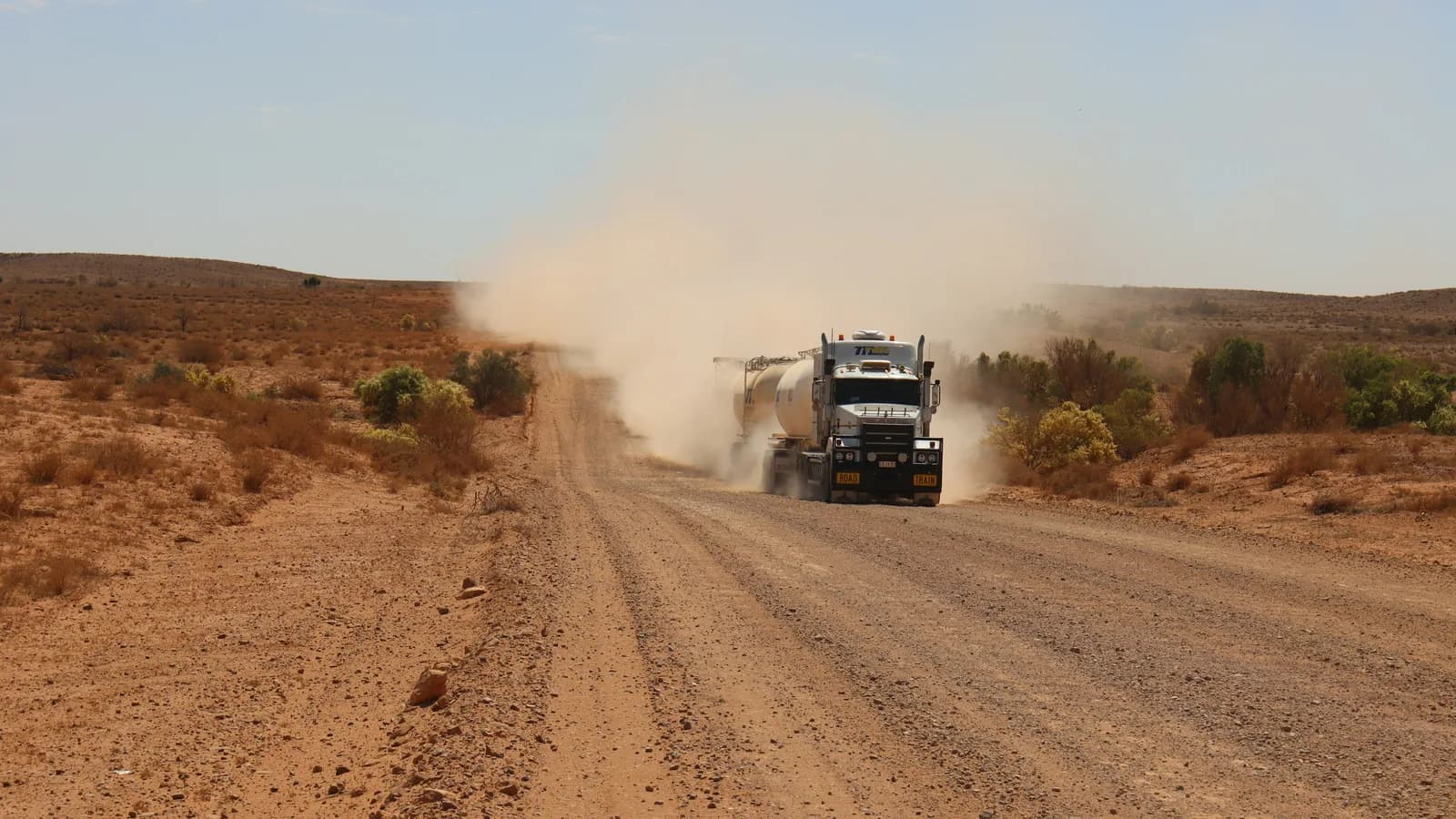 A tanker road train trailing a long dust cloud along an unsealed outback road