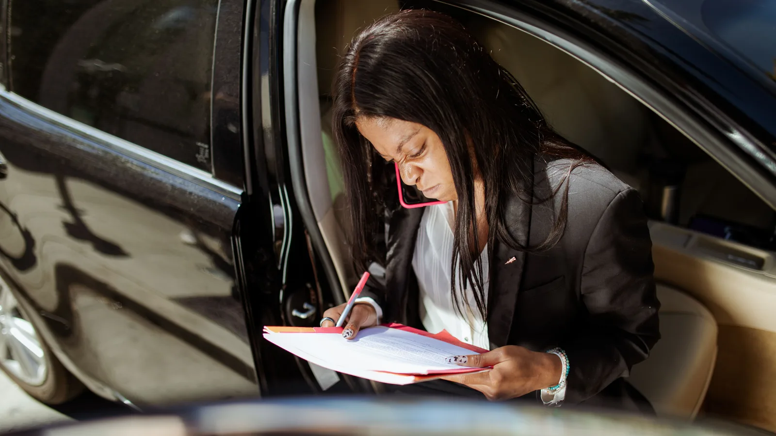 A woman seated in an open car doorway reading through printed paperwork