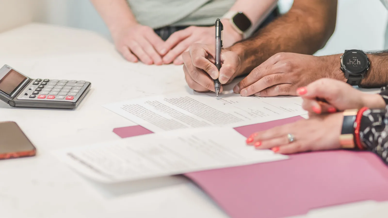A couple signing a loan contract at a table with a calculator and phone beside them