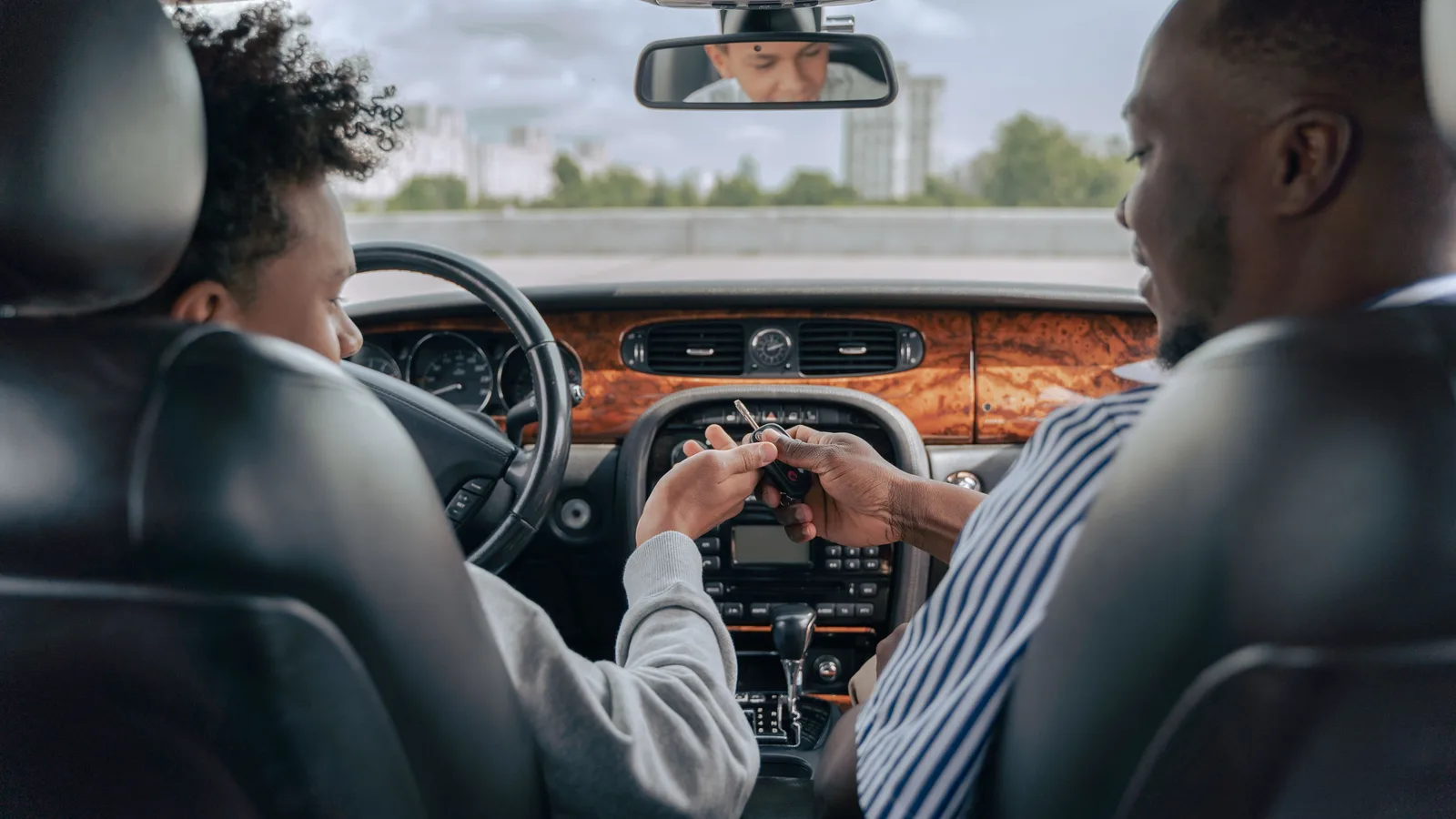 A salesperson passing car keys to a buyer sitting in the driver's seat