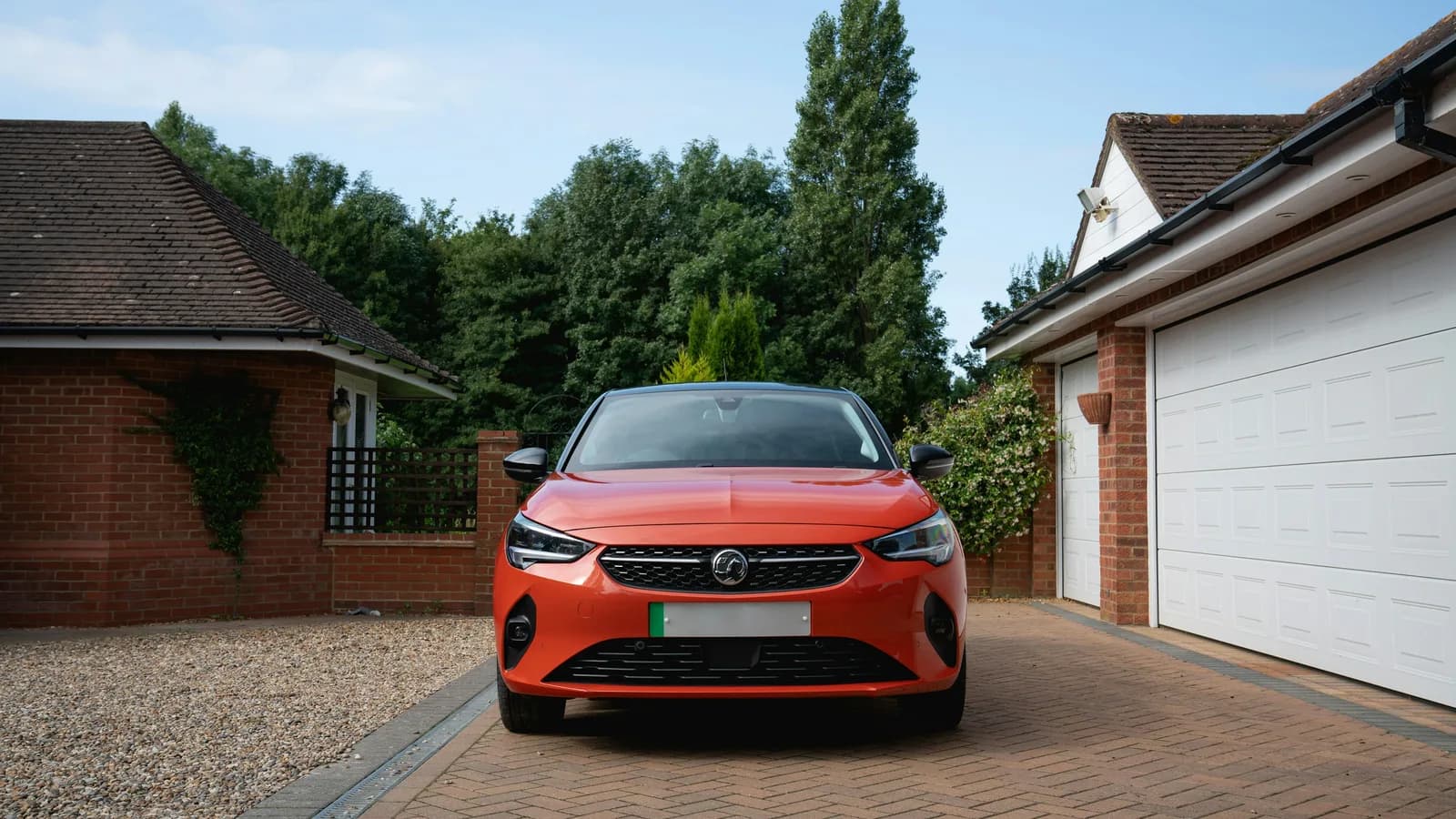 An orange hatchback parked on a suburban driveway between two houses