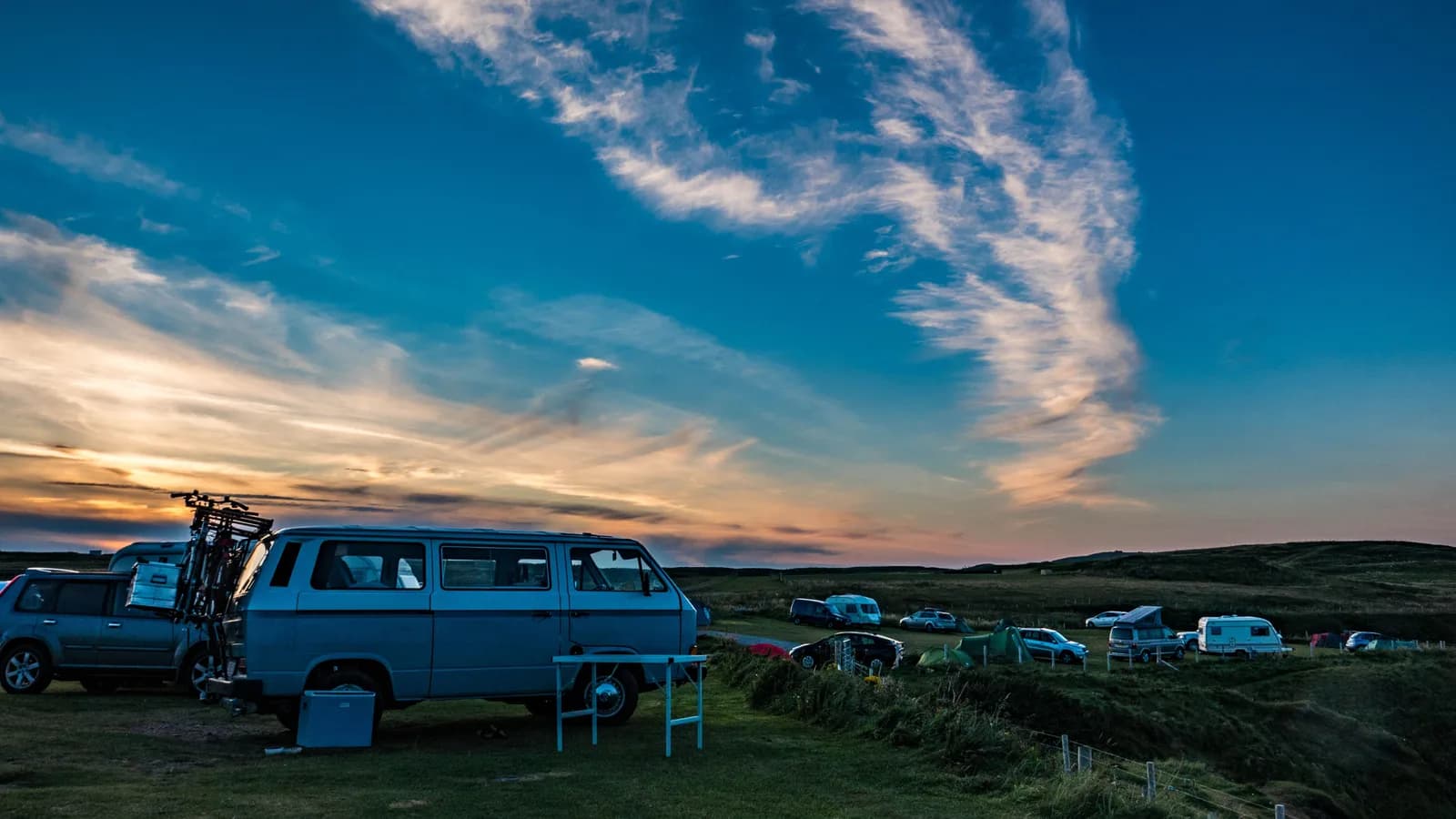 A campervan and caravans parked on a grassy coastal campsite at dusk