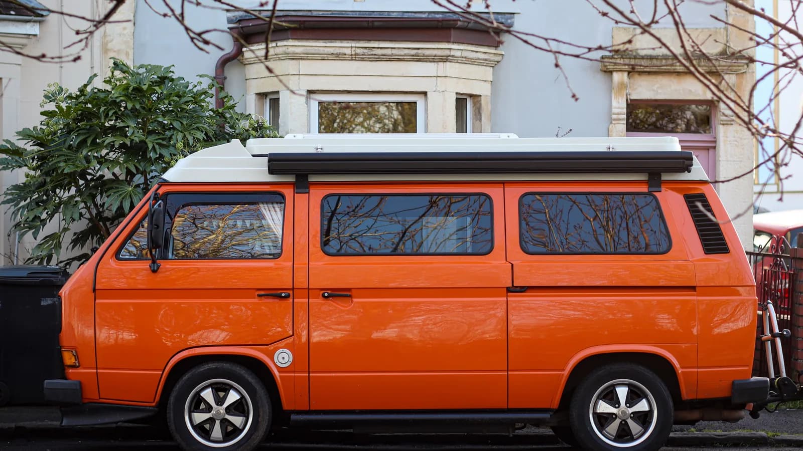 An orange VW campervan with a roof pod and side awning parked on a suburban street