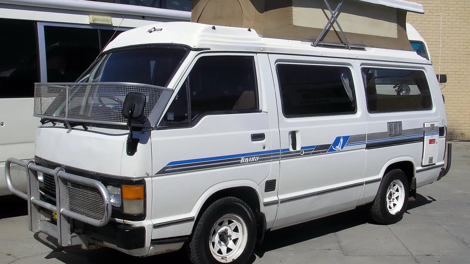 A white Toyota HiAce campervan with a raised pop-top roof parked outdoors