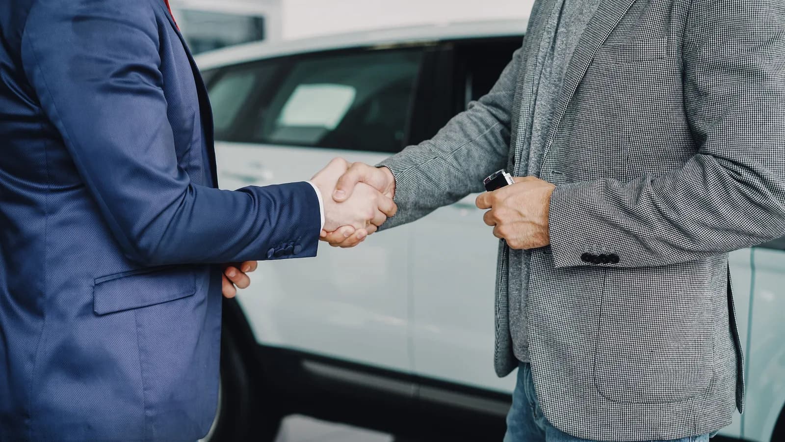Two people exchange car keys beside a vehicle after agreeing on a sale