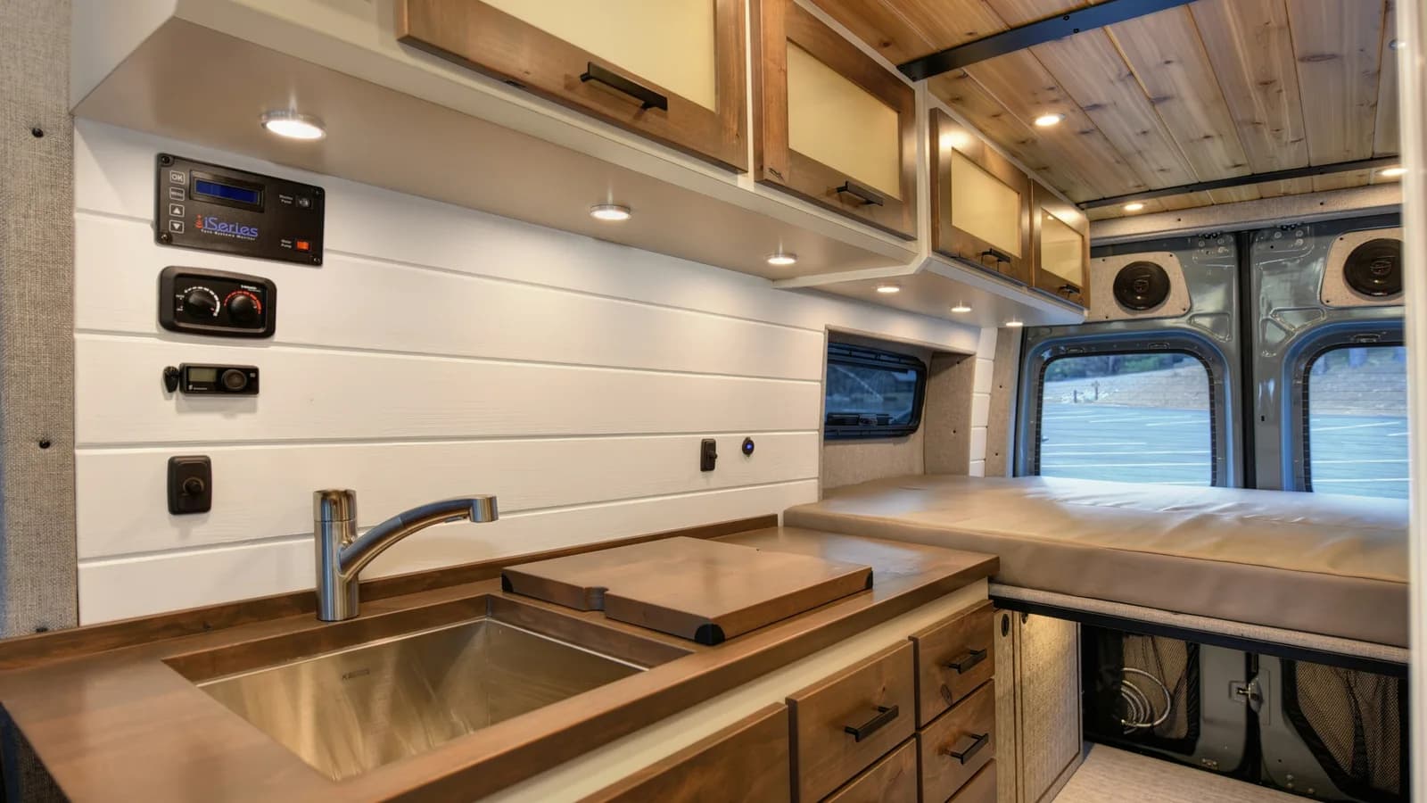 Finished van conversion interior with sink, timber benchtop, cabinets, wall-mounted electrical control panel and bed platform