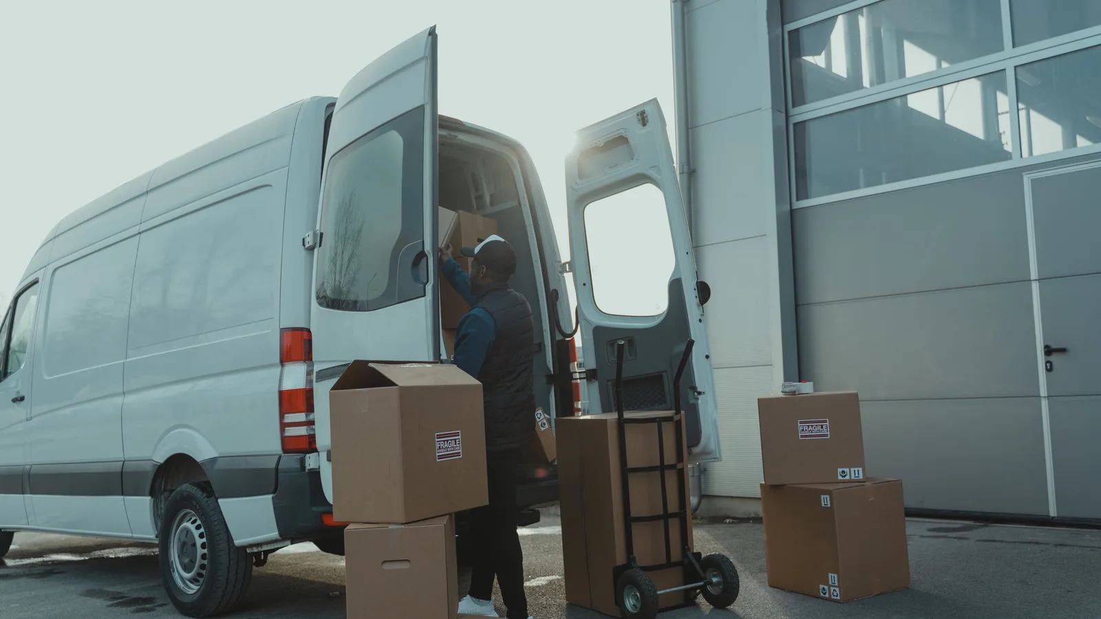 A courier lifting cardboard boxes out of the open rear doors of a white work van