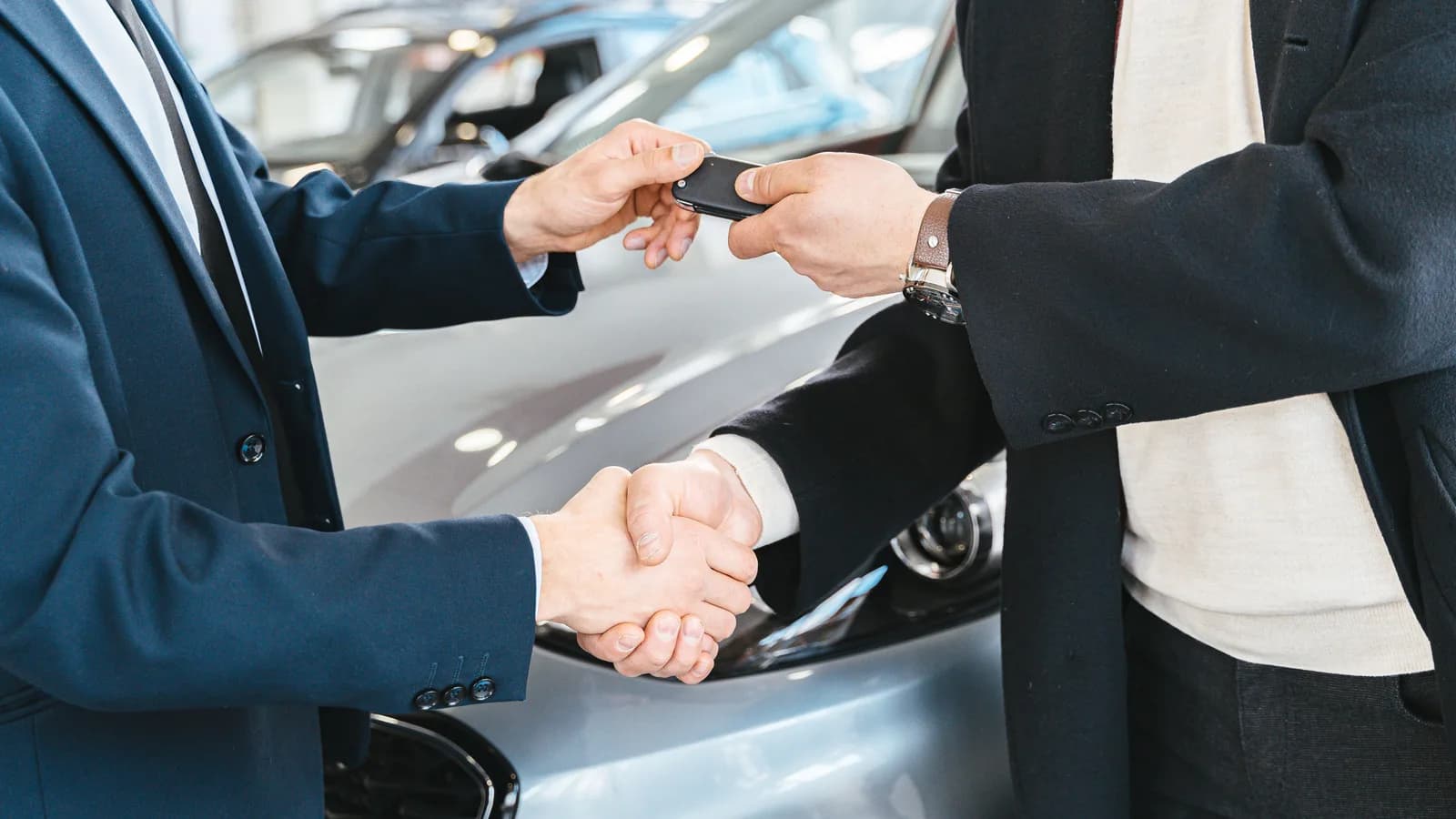 Two people shaking hands as one passes car keys beside a parked vehicle