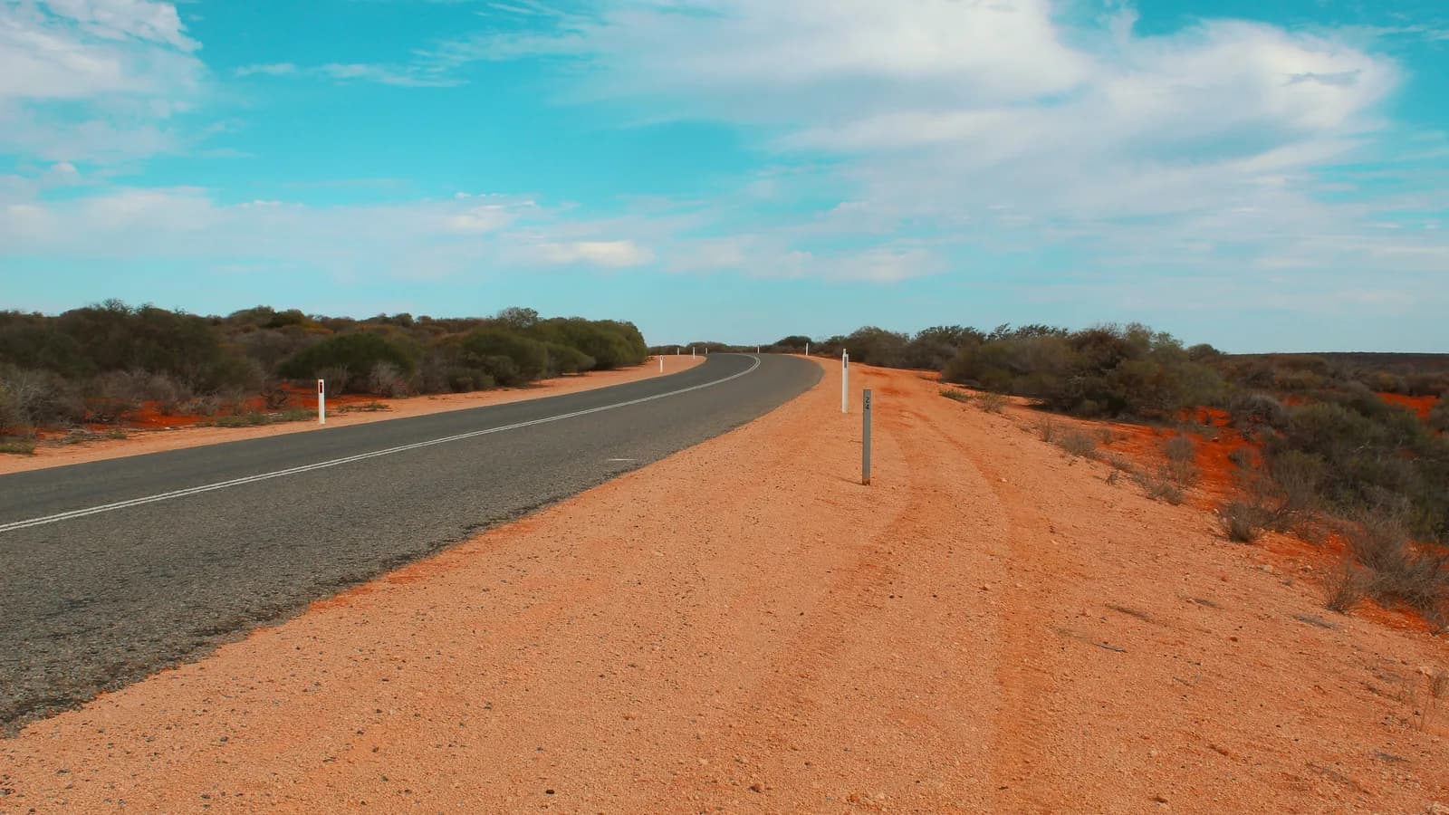 An empty sealed road running to the horizon across red outback country under a wide sky